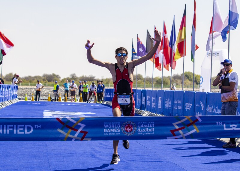 Male triathlete about to cross the finish line while celebrating already with his hands up