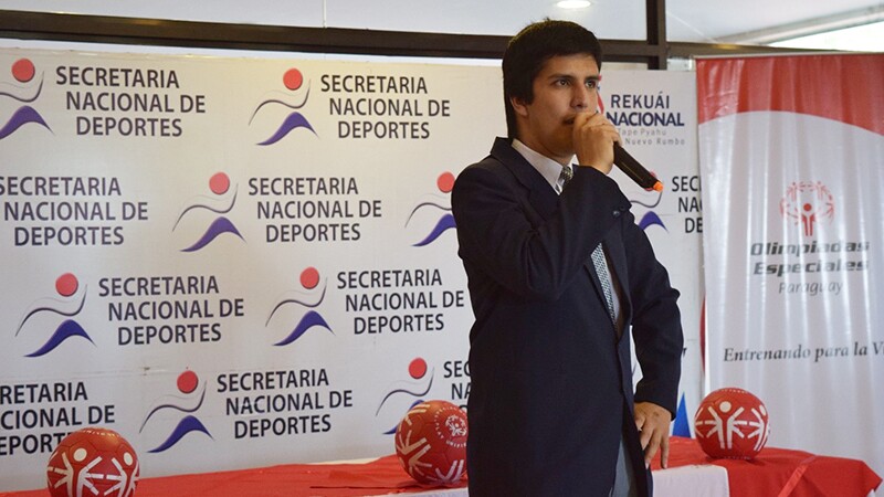 Young man holding microphone speaking to group of people.