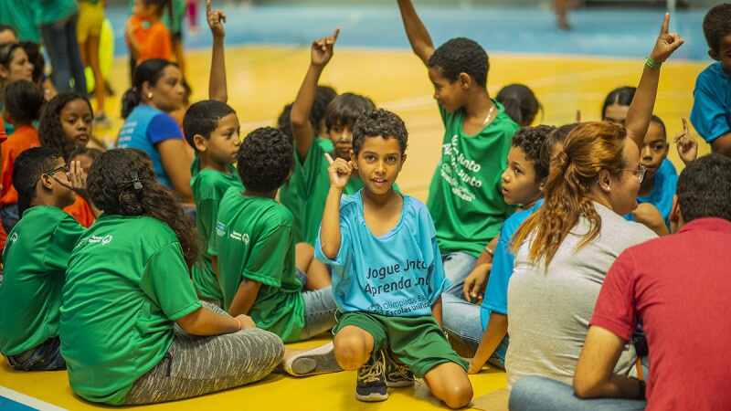 Young children sitting in a group on a gym floor. 