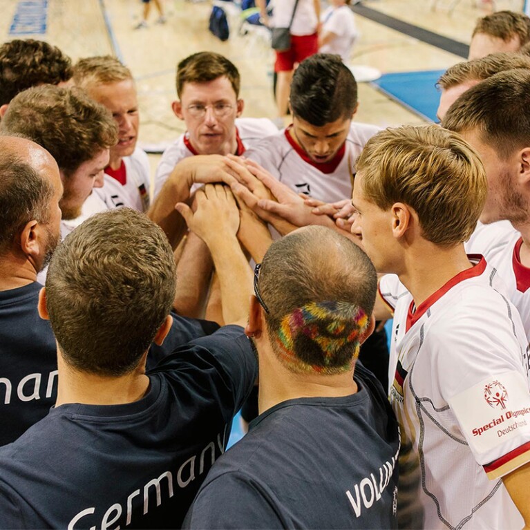 A group of players on a court standing in a circle with all their hands in together. 